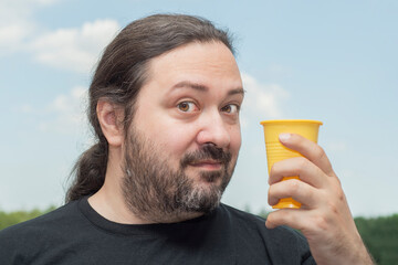 Fototapeta premium An adult man with a beard shows an empty, yellow plastic cup. Man on a light background.