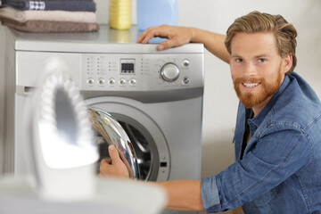 Fototapeta na wymiar man is loading clothes or fabric into washing machine