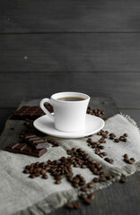 Coffee cup with cookies and chocolate with scattered coffee beans on linen and wooden table background. Mug of black coffee.