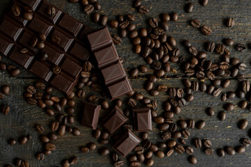 Roasted arabica coffee beans scattered on a wooden table with a bar of dark chocolate. Fresh coffee beans.