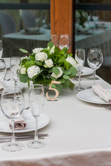 A white and green bouquet of flowers in a golden vase stands on a festive table close-up. Number five. Served table