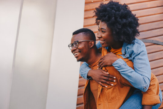 Young gorgeous hipster african couple having piggyback outdoors and having great time.