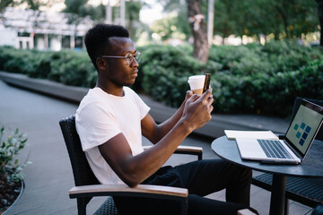 Fototapeta premium Black man with coffee browsing smartphone in street cafe