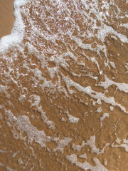 Wave with foam on the sandy beach