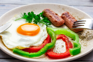 sunny side up. Fried eggs with sausages and vegetables on a light wooden table.