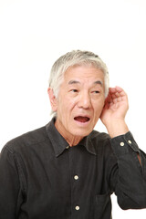 senior Japanese man with hand behind ear listening closely
