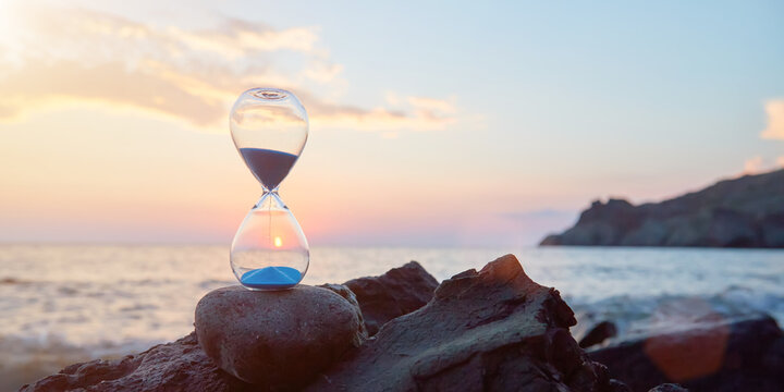 Hourglass with blue falling sand inside. Ocean landscape and golden hour. Time fly and need in rest concept, copy space