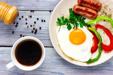 sunny side up. Fried eggs with sausages, vegetables and cup of coffee on a light wooden table. Top view