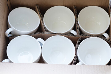 porcelain, white cups are packed in a brown box. Moving, closing restaurants during a pandemic. End of work, dismissal. Dishes in a box