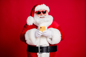 Portrait of his he nice handsome focused cheerful bearded Santa using device 5g blogging typing congratulation congrats web app store shop isolated bright vivid shine vibrant red color background