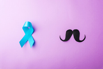 Black mustache paper and light blue ribbon, studio shot isolated on purple background, Prostate cancer awareness month, Fathers day, minimal November moustache concept