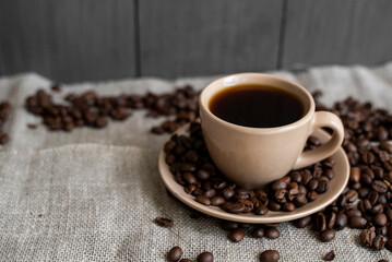 Coffee cup with roasted coffee beans on linen background. Mug of black coffe with scattered coffee beans. Fresh coffee beans.
