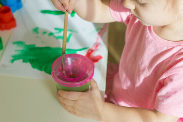 Little girl dipping paintbrush into a glass  with water and drawing the picture.