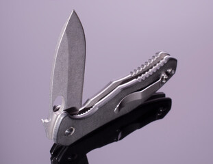 open folding pocket knife with textured black composite plastic cover plates on steel handle isolated on dark background with reflection on glossy surface.