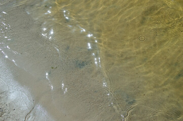 the surface of the river near the sandy shore with small waves and sun glare - a natural background