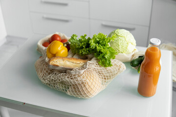 Eco friendly canvas grocery bag. Vegetables, fruits in reusable eco cotton bags and orange juice in a glass bottle on table. Zero waste shopping concept. Multi-use, reuse, recycle.