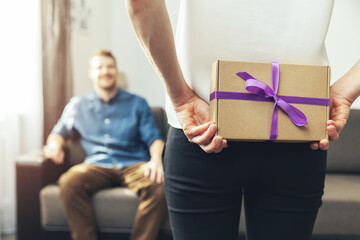 woman hiding surprise present behind back to beloved man at home