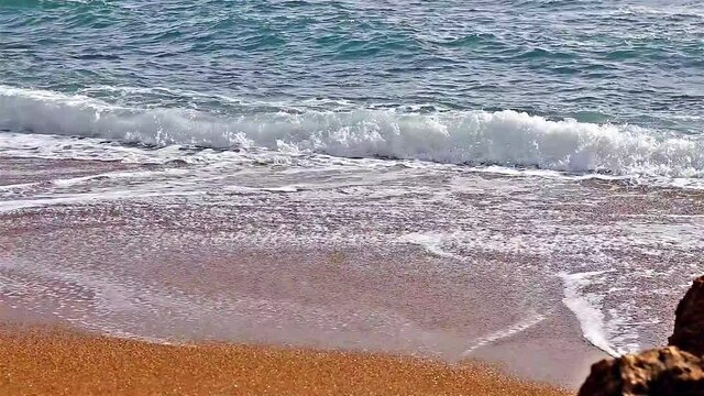 Waves of light blue water at a sandy beach in Greece. Ripples are travelling faster to approach a beach. Beautiful footage of wavy water medium on a sunny day. Close uo