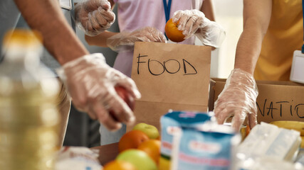 Close up of hands of volunteers in gloves collecting, sorting food for needy people in paper bags, Team working together on donation project