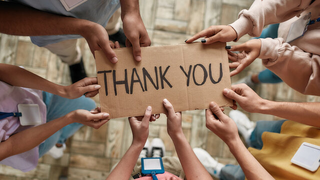 Top view of diverse young volunteers holding card with Thank you lettering while standing in charitable organization office