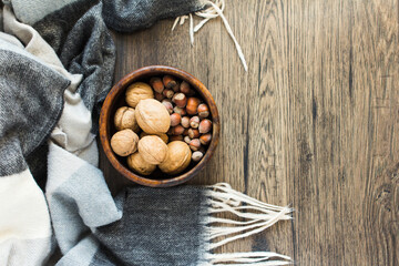 Wooden cup with nuts on a wooden background, next to a plaid