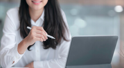 Cropped shot of young beautiful businesswoman holding stylus pen and working with tablet while sitting at office desk.