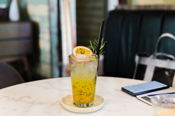 Fresh passion fruit juice in glass with green leaf and cell phone on table.
