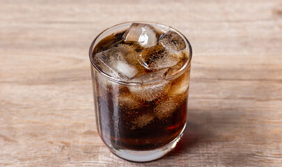 Close up cola and ice cube in clear glass on wooden table