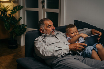 grandfather and grandson relaxing on sofa and using tablet at home