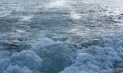 Light blue and white foamy relaxing waves behind power boat, in late summer.