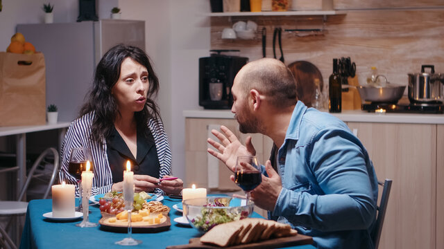 Happy Pregnant Woman Dissapointed By Husband During Romantic Dinner Showing Positive Test. Unhappy, Nervous, Angry Man Fighting With Wife, Unwanted Baby, Frustrated For Results.