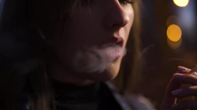 Close view: Young woman smokes cigarette at night