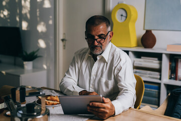 mid aged man having breakfast at home and using tablet computer