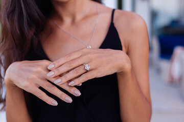 Close up of elegant diamond ring on woman finger. Woman wearing black dress. Love and wedding concept. Soft natural day light and selective focus.   