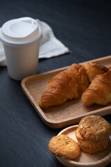 Breakfast with cookies and croissant on the wooden plate and hot coffee cup on stone table