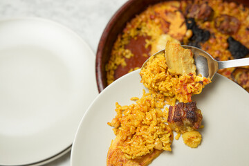Man's hands serving oven-baked rice on a plate with a spoon. Valencia, Spain