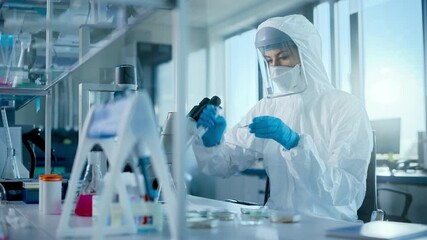 Beautiful Female Medical Scientist Wearing Coverall and Face Mask Using Micro Pipette while Working with Petri Dish. Vaccine, Drugs Research and Development Innovative Laboratory Modern Equipment  - Powered by Adobe