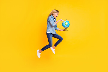 Full length body size photo of amazed jumping high schoolgirl keeping globe pointing on continent shouting amazed isolated on bright yellow color background