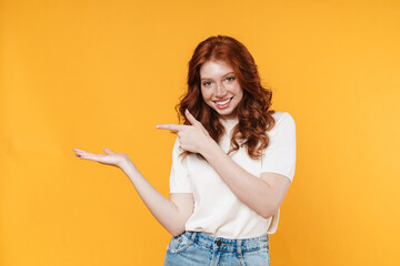 Image of ginger joyful girl holding and pointing finger at copyspace