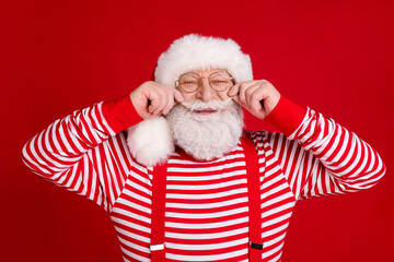 Photo of pensioner old man hands play mustachio entertain public audience mall promoter wear santa costume suspenders spectacles striped shirt headwear isolated red color background