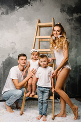 Smiling mom and dad with daughter, son on the floor. Fashion models with feathers. Happy family portrait in casual style clothes. Nice family wearing jeans isolated on grey wall.
