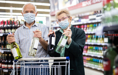 mature european spouses chooses bottle of wine in alcohol section of supermarket