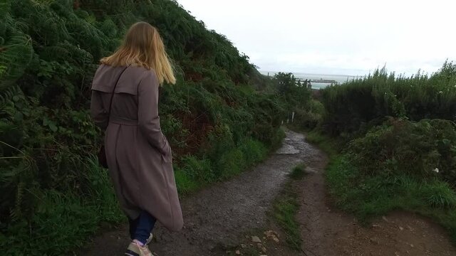 The girl in long coat walks down the hill. View of a young woman from the back. Tracking in Ireland near Dublin. High quality FullHD footage video.