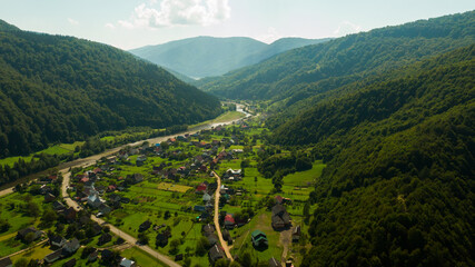 Fototapeta na wymiar small valley in the mountains, with the light of dawn illuminating the village with river. Mountains with little fog and haze, and clean blue sky. Aerial view
