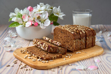 Dark multigrain bread made from rye, wheat, oats and barley with sunflower and flax seeds. Milk, apple tree flowers and light wooden rustic table.