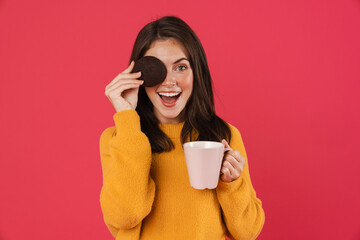 Image of excited girl making fun with cookie while drinking coffee
