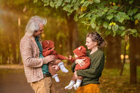 Mom And Dad Walk In Autumn Park With Twin Babies, Hold Babies In Their Arms.