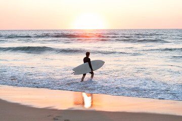 surfer man with the board in his arms entering the sea at sunset