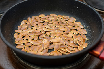 Part of a frying pan with pumpkin seeds in a shell on an electric stove