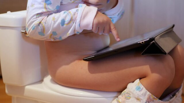 Little girl poops on toilet-shaped potty using tablet to relax.